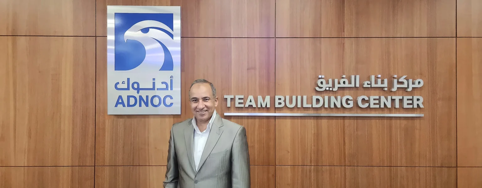 Mostafa Azzam standing between the ADNOC logo and the Team Building Center sign, Abu Dhabi